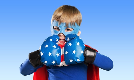 Superhero kid wearing boxing gloves against blue sky background. Girl power and feminism conceptの写真素材