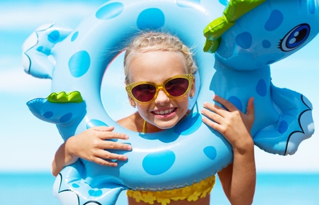 little girl in swimsuit playing with an inflatable whale on the beach resortの写真素材