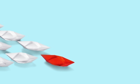 Leadership concept with paper boats on blue wooden background. One leader ship leads other ships. Filtered and toned imageの写真素材