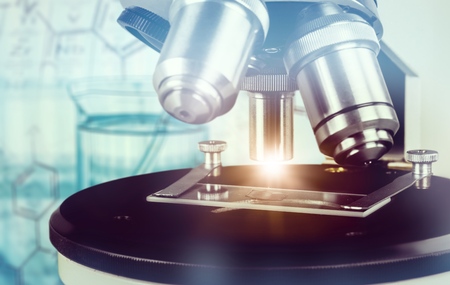 Scientific background with closeup on light microscope and laboratory out of focus. This image is...