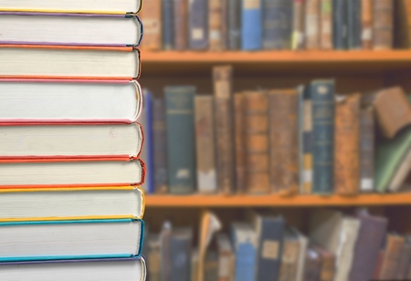 Book stack on wood desk and blurred bookshelf in the library room, education conceptの写真素材