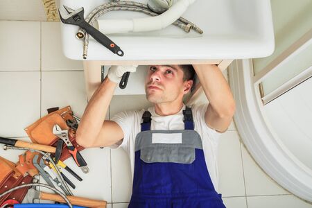 High Angle View Of Male Plumber In Overall Fixing Sink Pipe