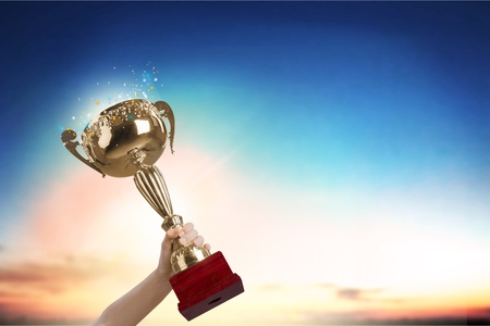 Man holding up a gold trophy cup with abstract shiny background, copy space for textの写真素材