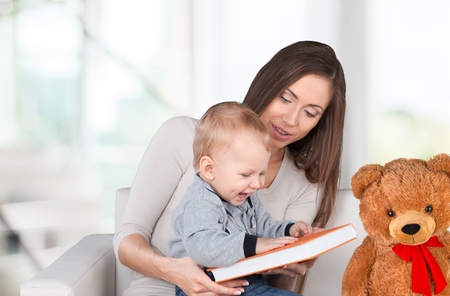 Mother reading a book a little baby daughter on the sofa at home