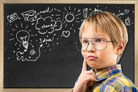 Portrait of a schoolboy in big round spectacles and academic hat at a classroom.の写真素材