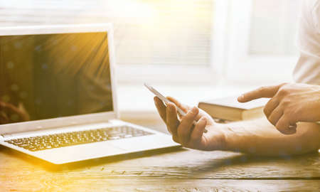 designer hand working and smart phone and blank screen laptop on wooden desk in office with london...