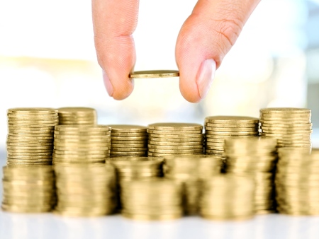 Savings, close up of male hand stacking golden coins over sky background