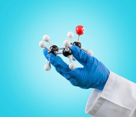 hand in blue rubber glove and white lab coat holding a 3d model of a mollecular structure made of...