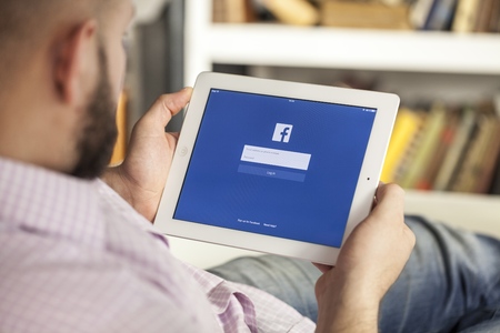 KHERSON, UKRAINE - FEBRUARY 19 :man withfacebook on  tablet pc in the hands on background