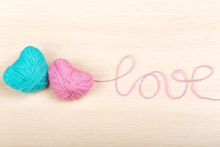 Two pink clews in shape of heart with word  &quot;love&quot; made from yarn on  white wooden backgroundの写真素材