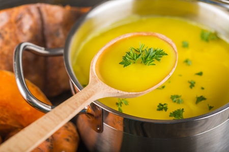 Homemade carrot soup in a pot with a wooden ladleの写真素材