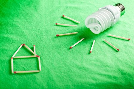 Compact flourescent bulb and matchsticks that make up a house and rays of light - energy saving conceptの写真素材