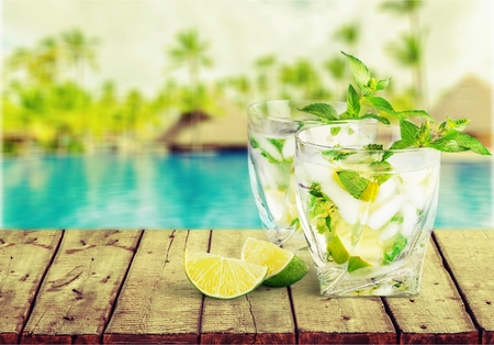 Fresh mojito drink placed on wooden planks, blur tropical beach on background. Summer drinks and beach vacation backgroundの写真素材