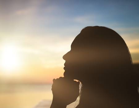 Silhouette woman prays at sunsetの写真素材