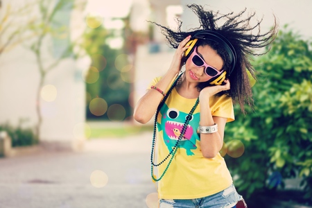 Excited girl dancing and listening music with headphones and smart phone in the street with hair...