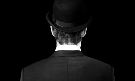 Man posing in the dark with a fedora hat and a trench coat, 1950s noir film style characterの写真素材