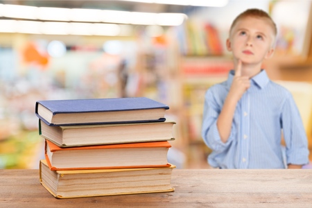 Back to school and happy time! Cute industrious child is sitting at a desk indoors. Kid is learning in class on background of blackboard. Girl reading the book.の写真素材