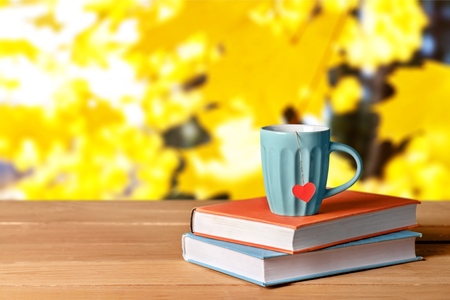 blue cup with red heart on green and orange books on grunge wooden tableの写真素材