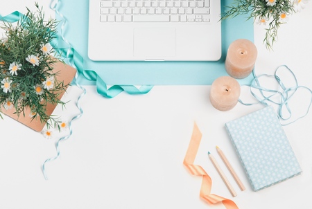 Workspace with paintbrush, laptop, lilac flowers bouquet, spool with beige and blue ribbon, mint diary on white background. Flat lay, top viewの写真素材