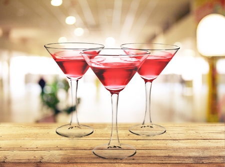 Three colorful cocktails in large wine glasses in a classic bar environment with dozens of blurry liquor bottles in the background.の写真素材