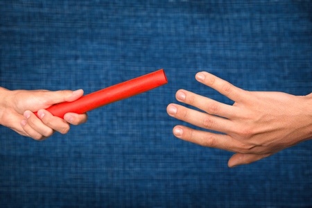 Close-up of relay baton being passed on town background.Teamworkの写真素材