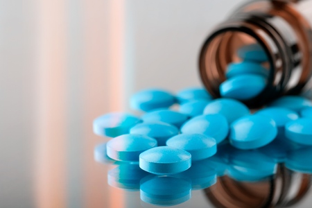 closeup of the desk of a doctors office with a bottle with pills in the foreground and a stethoscope in the backgroundの写真素材