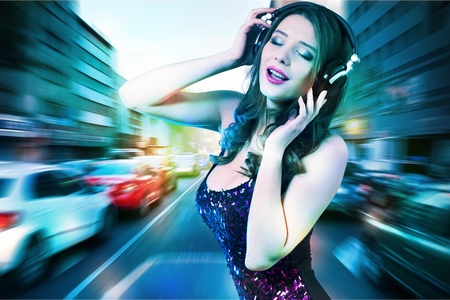 Excited girl dancing and listening music with headphones and smart phone in the street with hair...