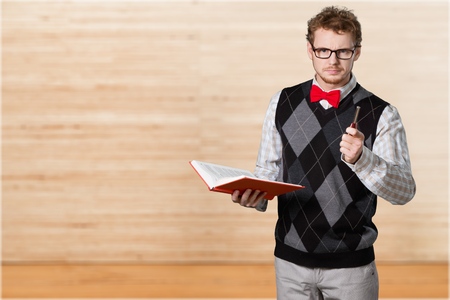 Closeup portrait of a senior elderly  teacher holding a book and a pen, looking very serious, unhappy and grumpy, isolated on white background. Human emotions and facial expressions. Education conceptの写真素材