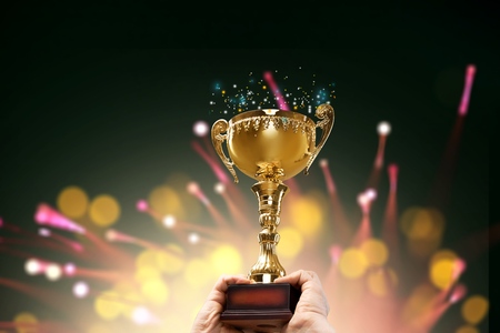 Man holding up a gold trophy cup with abstract shiny background, copy space for textの写真素材