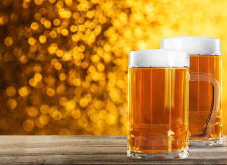 Two Nice Glasses of Beer in right on the wooden rustic table with orange bokeh and confetti effect background for carnival.の写真素材