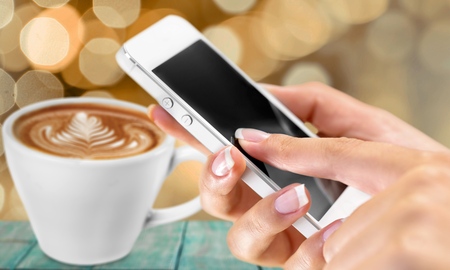 Hands using Iphone7 Plus jet black color with icons of social media on screen with latte art,...