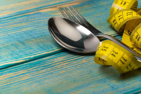 Measuring tape wrapped around fork lying on color surface. Diet conceptの写真素材