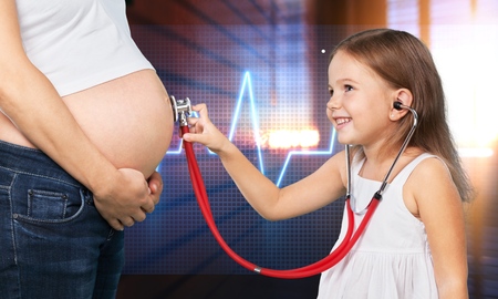 kid girl examining pregnant mothers tummyの写真素材