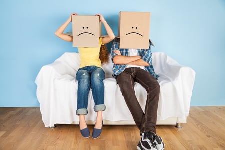 couple sitting on couch with moving boxes on head having fun togetherの写真素材