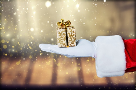 Christmas Santa Claus showing empty copy space on the open hand palm for text. Proposing product. Advertisement gesture presenting point. Holding gift, text or product over wooden background.の写真素材