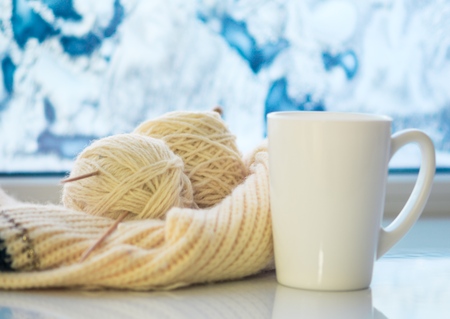Cozy winter still life: mug of hot tea and warm woolen knitting on vintage windowsill against snow...