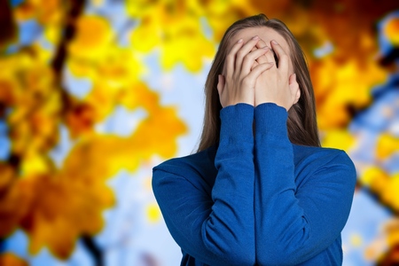 one sad woman sitting on the floor near a wall and holding her head in her handsの写真素材