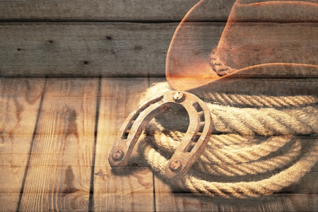 American West rodeo old horseshoe on lariat lasso and roping work gloves with Western horse rider gear with hat and aged leather roper boots on antique wood boars in a ranch barnの写真素材