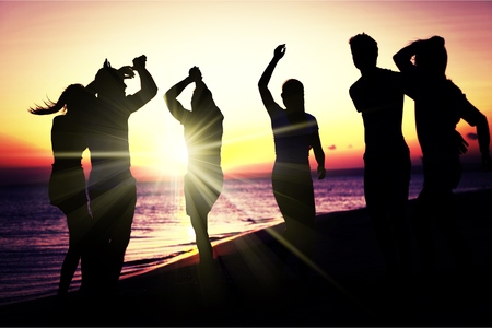 People (two couples) on the beach having a party, drinking and having a lot of fun in the sunset (only silhouette of people to be seen, people having bottles in hands with the sun shining through)の写真素材