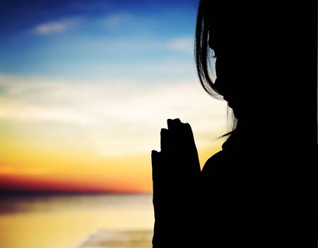 Silhouette woman prays at sunsetの写真素材