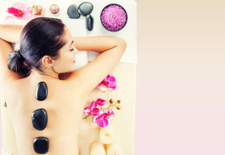 Adult woman relaxing in spa salon with hot stones on body. Beauty treatment therapy