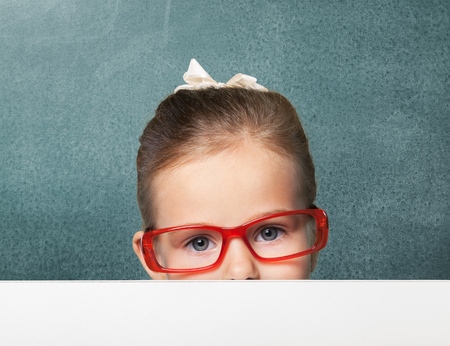 Serious boy in red-framed eyeglasses looking up from behind the table, close-up shotの写真素材