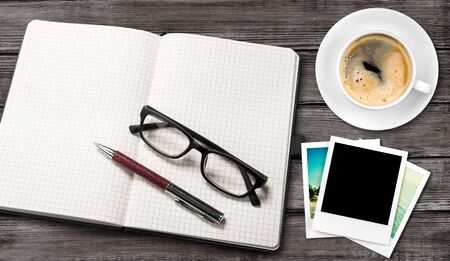 top view of open blank notebook and travel  photographs next to cup of coffee over wooden table....