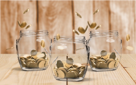 Savings rate concept - jars in row filling up with falling coins, focus on middle jar