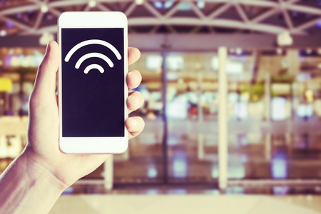 Close-up of hand holding smartphone with free WiFi hotspot icon on the screen to connect to wireless...