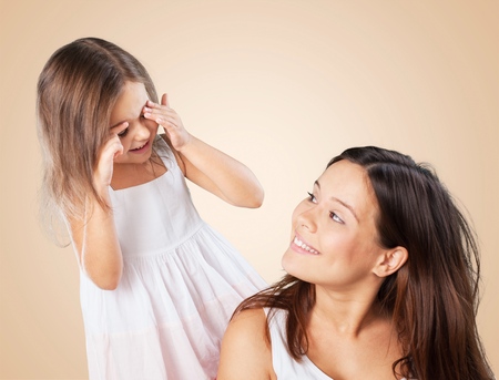 Young daughter closes hands eyes mom - isolated. Happy family people concept.の写真素材