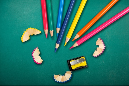 some colored pencils of different colors and a pencil sharpener and pencil shavings on a white...