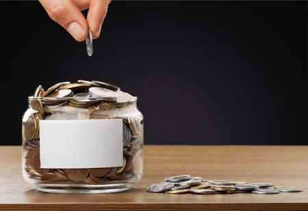 Hand putting coins in jar with money