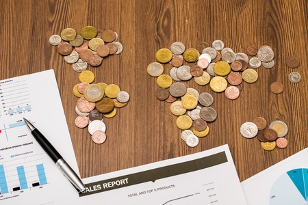 Office desk with world map made of money coins and report sheets