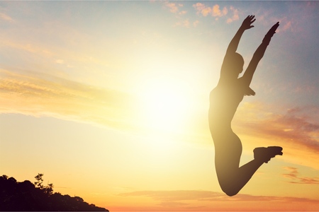 Silhouette of happy joyful woman jumping and having fun at the beach against the sunset. Freedom and...